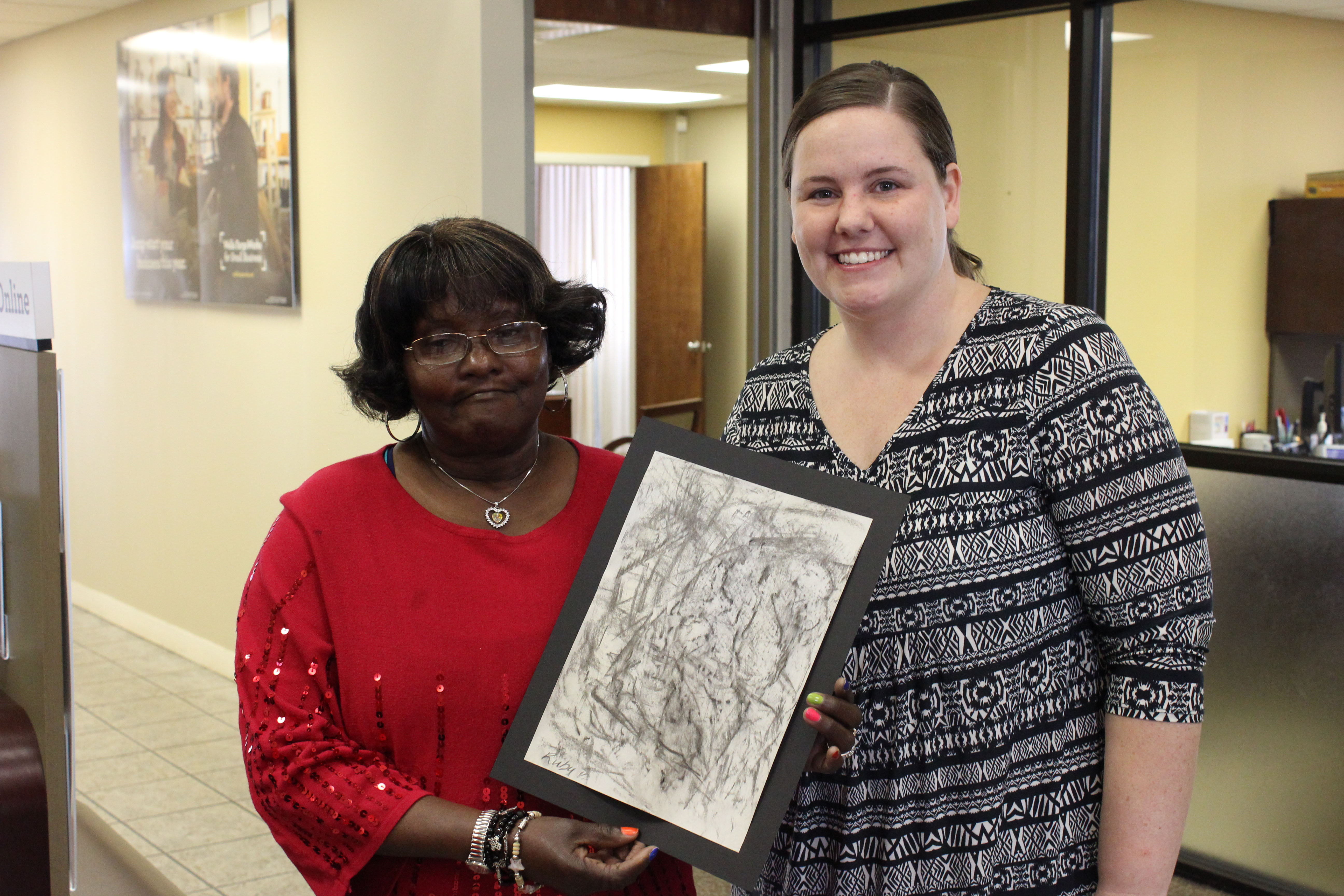 Sunland resident Ruby P., left, proudly displays her willow charcoal rubbing with a Wells Fargo employee.